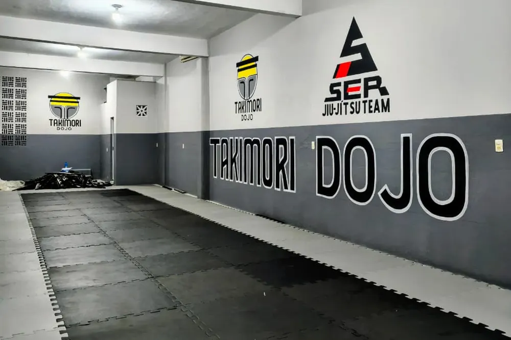 Tatame do TAKIMORI Dojo vazio, com a parede grafitada TAKIMORI DOJO ao fundo
