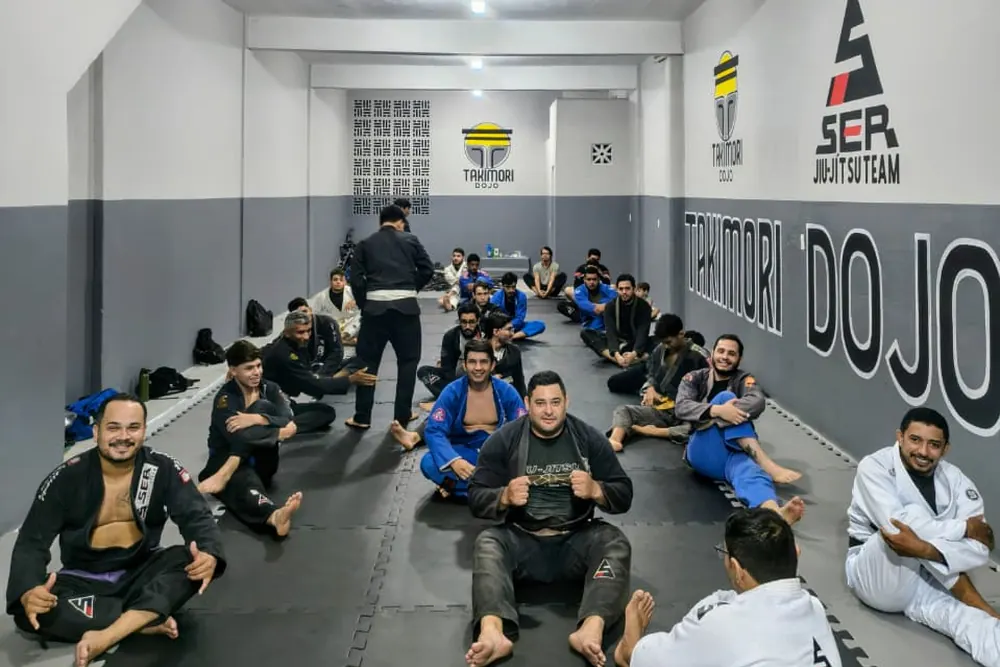 Alunos sentados no tatame durante a aula, em roda