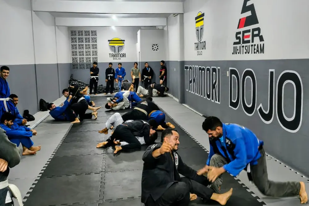 Treino de Jiu-Jítsu em andamento, alunos praticando em duplas