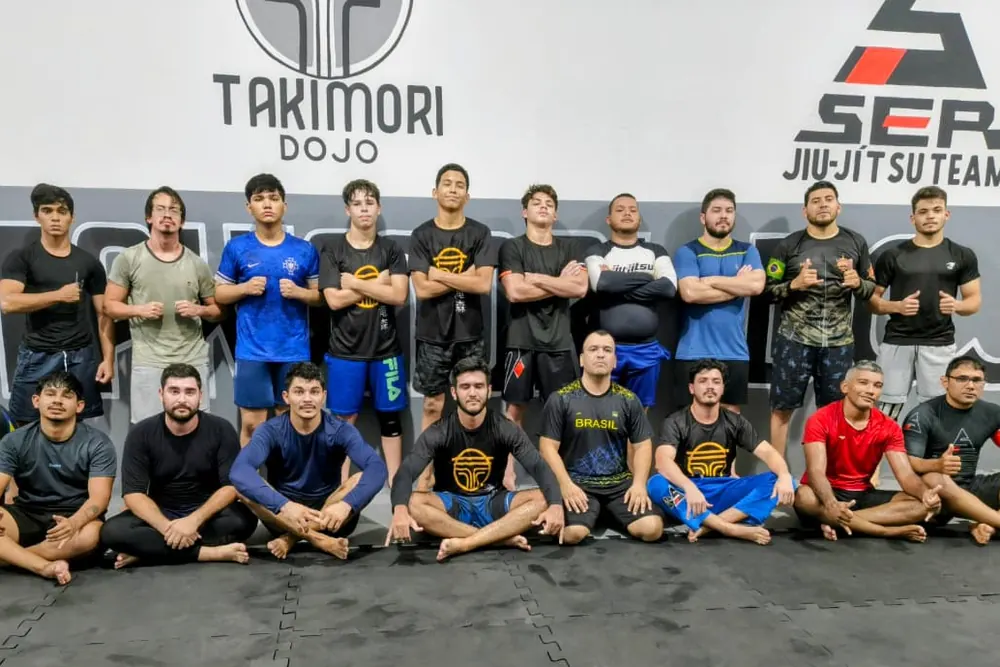 Foto da turma do dojo em frente aos símbolos TAKIMORI e SER Jiu-Jítsu Team